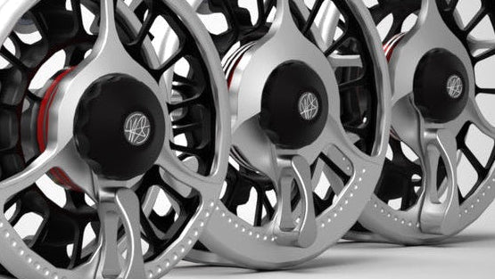 Three metallic fly fishing reels on a light gray background